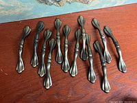 Twelve metal door pull poles laid out side by side on a wooden surface, showing entire lot.