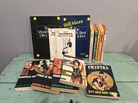 Photo of lot showing an assortment of adult-themed books including humor and espionage titles, both in French and English, arranged on a table.