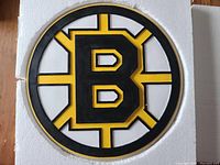 Front side of a round Boston Bruins wall logo sign with black, yellow and white raised logo design.
