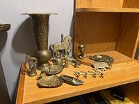Full view of brass collection on wooden shelf including large vase, animal dishes, figurines, wall hooks