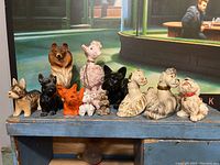 Front view of 12 dog figurines in various colors including ceramic pink poodle, brown collie, orange schnauzer, black cast iron schnauzer and small poodles.
