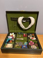 Overhead view of the vintage gray box with green velvet interior, showing the assortment of costume jewelry including pins, earrings, pendants, and necklaces on the removable tray and hanging bar.