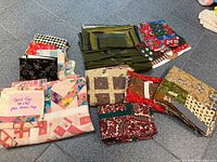 Overview photo showing multiple bundles of unfinished quilt pieces arranged on floor, including green quilt, Christmas fabric pieces, and others.