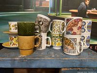 Photo showing all six sets of mugs stacked and arranged in pairs with visible detailed designs including embossed and printed patterns.