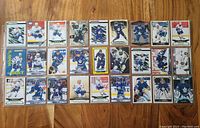 27 Toronto Maple Leafs hockey cards laid out in rows showing various players including Auston Matthews, William Nylander, and Matthew Knies. Cards are predominantly white and blue with multiple designs.