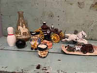 Group of vintage decorative items including ceramic figurines, salt and pepper shakers, glass vase, and miniature carriages on blue surface