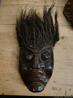 Front view of the dark carved wooden tribal mask with facial features and attached black hair.