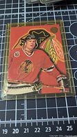 Photo of individual hockey card in protective case showing player in Chicago Blackhawks jersey with Leaf Studio branding and orange background.