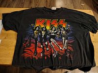 Front view of black vintage Kiss T-shirt with colorful graphic of the Kiss band members in stage makeup and costumes.