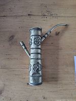 Front view of the antique Tibetan opium pipe showing floral embossed decorations and attached spouts.