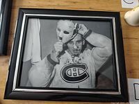Front view of the framed 8x10 black and white photo of Jacques Plante putting on his goalie mask, showing the Montreal Canadiens sweater and mask detail.