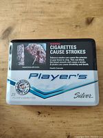 Front of the Player's Silver metal cigarette tin showing health warning and branding.