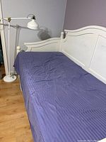 White wooden daybed with blue bedding and white pole floor lamp in corner of room