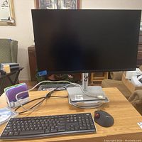 Front view of Dell monitor on a desk with Logitech keyboard and trackball mouse, cables, and CDs