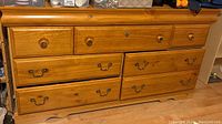 Front view of wood dresser with multiple drawers and mixed hardware, showing scratches and wood grain texture.