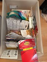 Photo showing a box containing several packages of Command hooks, tape, clear plastic containers, and party supplies.