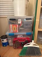 Photo of stacked storage totes labeled 'PPE Handheld Electrical Tools', with a 1-gallon Kilz paint can to the side, a red battery kit on floor, white bucket and green-handled broom with two-tone bristles.