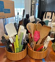 Photo showing three wooden revolving holders filled with various kitchen utensils including spatulas, wooden spoons, knives, peelers, and tongs.