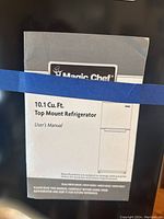 Manual for Magic Chef 10.1 Cu Ft Top Mount Refrigerator taped to black surface.