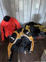 Three motorcycle jackets displayed, one black and yellow Joe Rocket with #69 emblem, one orange and black Olympia Moto Sports, and another yellow and black jacket, along with black gloves and tote.