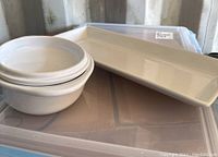 White rectangular ceramic serving plate alongside three white bowls arranged on top of a clear plastic tote container