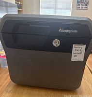 Front view of Sentry Safe with keyhole and brand logo visible, showing approximate dimensions 16x12x14 inches noted on sticker.