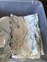 Folded floral sheets and quilts in a plastic bin showing blue and green floral vine designs