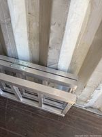 Top-down angled photo showing the folded tri-fold aluminum ramp ladder leaning against a wall, highlighting its triple sections and lightweight aluminum structure.