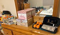 Wide view of all items on wooden dresser including boxed cars, painted wood cart, hand weights, decorative boxes, ebonite kit, and carrying case.