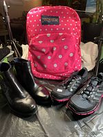 Pink JanSport polka dot backpack with white spots alongside black Dorking ankle boots and Adidas golf shoes.