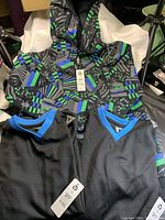 Photo of a black skull patterned boys hoodie with blue and green geometric accents alongside two black and blue short sleeve jerseys with V-necks.