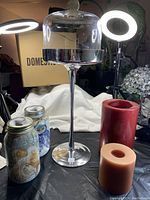 Photo showing a 20-inch tall silver metallic covered pedestal with a dome lid and textured knob, a red pillar candle, and a smaller peach-colored pillar candle.