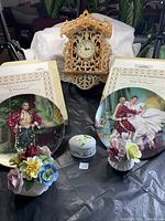 Overview of lot items including 2 King and I plates with certificates, wooden clock, 2 floral figurines, and small trinket box