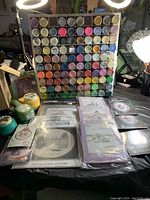 Organizer rack filled with many small jars of acrylic paint, assorted colors, plus needlepoint kits and craft punches in front.