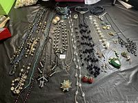Full view of assorted jewelry including necklaces, earrings, brooches, and a cuff bracelet on black cloth