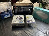 Photo of all 5 boxed items together on a surface: Lookee TV, Pit Stop air compressor, blue UV sterilizer box, shower radio, Leviton dimmer switch