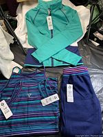 Photo showing teal and navy jacket with zipper, two striped tank tops in purple, teal and navy colors.