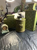 Photo showing two green geometric patterned urns, the elephant urn with metal lid, and the jade clock on a black surface