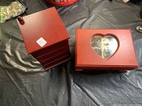 Two red wooden jewelry boxes, one square with drawers and one rectangular with heart-shaped glass window