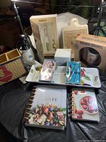 Photo of kitchen lot showing baking set, bamboo utensil stand, kids utensils set, cafe cup, recipe books and more on a black tablecloth.