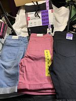 Top view of folded shorts including two pairs of black/grey XS pull-on shorts, pink shorts size 6, and black Buffalo jeans size 4.