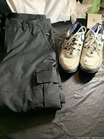 Photo of Bonfire black ski pants folded and FootJoy golf shoes side by side on black surface