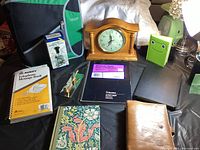 Photo of entire lot showing quartz clock, golf paperweight clip, various books, binder, numbering stamp, and organizers on black surface