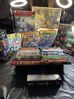 Full view of multiple jigsaw puzzles and a large collection of DVDs arranged horizontally on table surface.