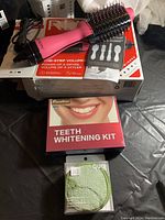 Photo showing Revlon one-step volumizer hairbrush on its box, Pankoo teeth whitening kit, and Quo bamboo cleansing cloths arranged on a black fabric surface