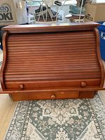 Wooden roll top desk closed, showing slatted roll top with three wooden knob handles, medium-toned wood, a few dings and large surface mark visible.