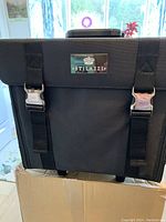 Front view of the black Stilazzi makeup case with straps, clasps, and logo plate.