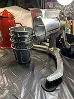 Side view of the metal manual 3-footed grinder with 5 blades and stacked metal parts next to it