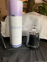 Photo showing Nova crystal clear water bottle in original packaging next to a black candle in a glass container with a rounded glass lid with crystals.