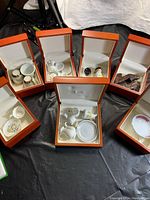 Seven small wood boxes open to display assorted miniature porcelain items including plates, cups, and vases.